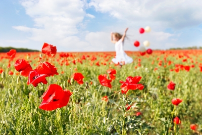 happy girl with colorful balloons running in poppy field